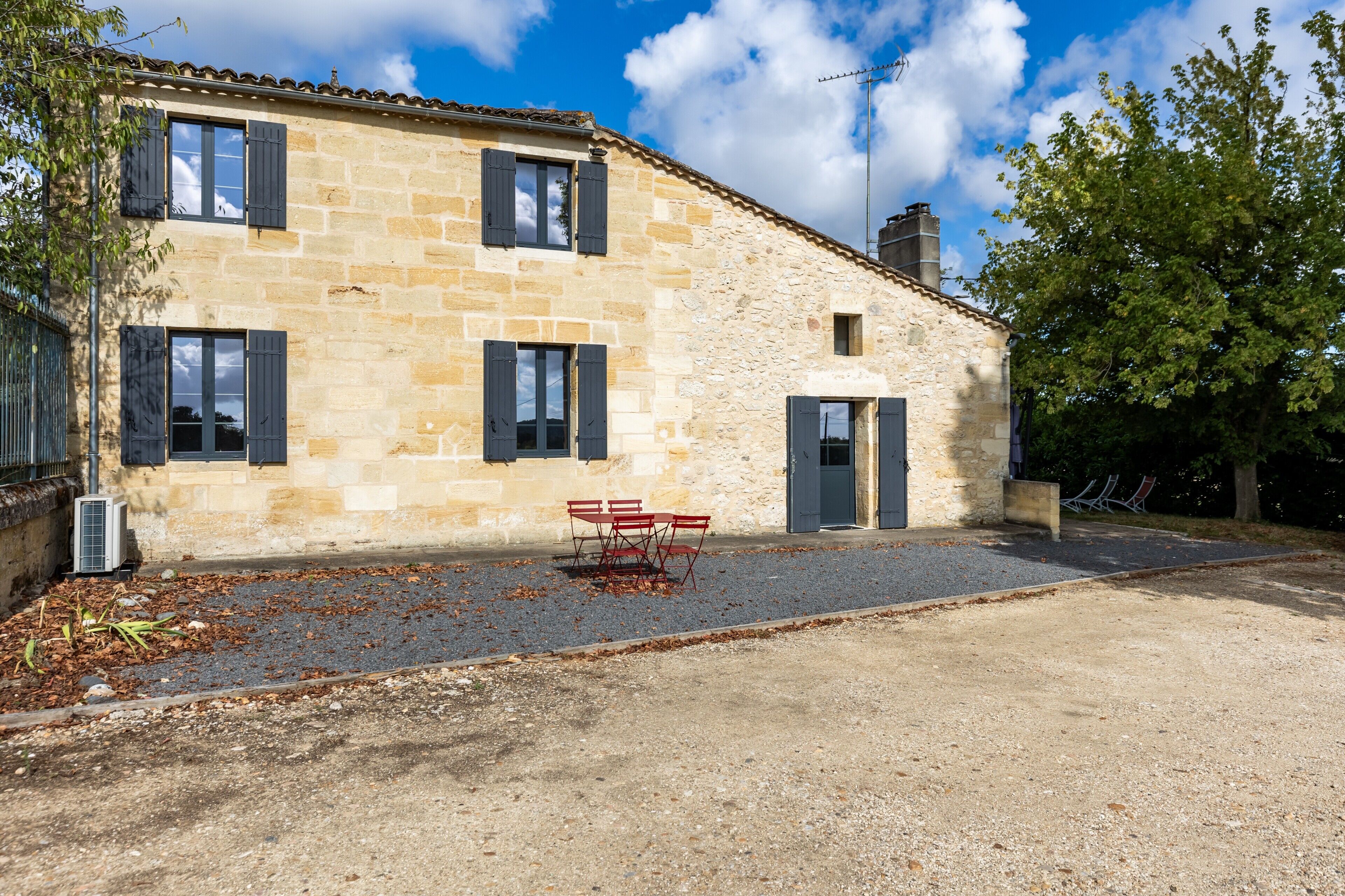 Un bâtiment en pierre avec une allée gravillonnée, une porte et une fenêtre avec des volets.