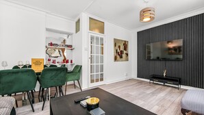 A modern living room with a dining area, a flat-screen TV, and a bookshelf.