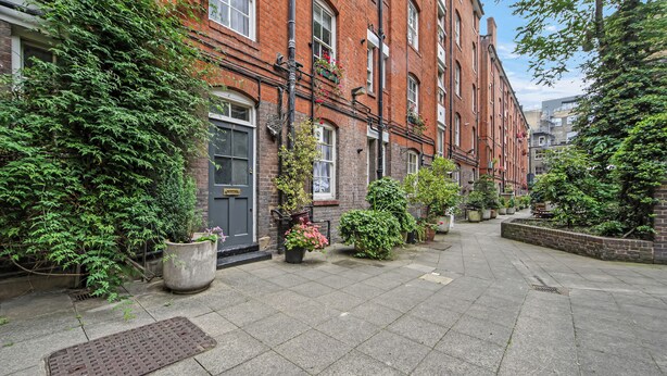 A narrow urban street with brick buildings, potted plants, and a clear sky.