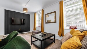 A modern living room with a flat-screen TV, a black entertainment unit, a coffee table, and a sofa with yellow cushions.