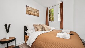 A bedroom with a bed, pillows, a nightstand, a window with curtains, and a painting on the wall.
