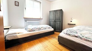 A bedroom with two beds, a radiator, a window with curtains, a wardrobe, and a bedside table.