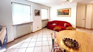 A bright living room with a red sofa, a wooden dining table with a decorative bowl, and a painting on the wall.