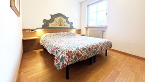 A bedroom with a wooden bed, a nightstand, a wall-mounted heater, and a window with curtains.