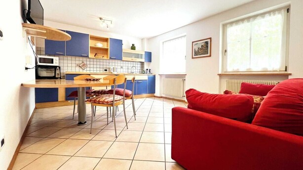 A compact living space with a kitchen area, a dining table, and a red sofa.