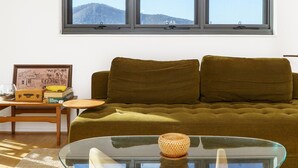 Ein Wohnzimmer mit einem grünen Sofa, einem Glastisch, einem gerahmten Bild und einem kleinen Holztisch mit Büchern und einem Glas.