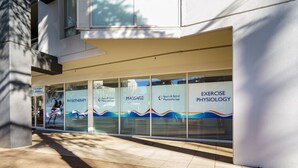 Ein Gebäudefassad mit großen Fenstern, die Dienstleistungen wie Physiotherapie, Massage und Trainingsphysiologie präsentieren.