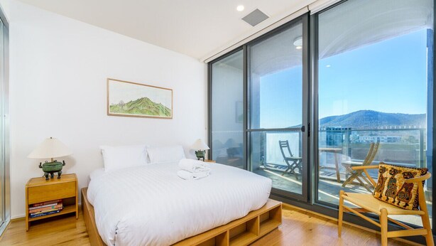 Ein Schlafzimmer mit einem Bett, einem Nachttisch, einem Sessel und einem großen Fenster mit Bergblick.