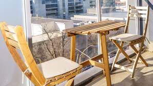 Ein Balkon mit Holzmöbeln, darunter zwei Stühle und ein Tisch, mit Blick auf eine Stadtlandschaft.