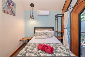 Een slaapkamer met een bed, nachtkastje, hanglamp, raam met gordijnen en een airconditioner.
