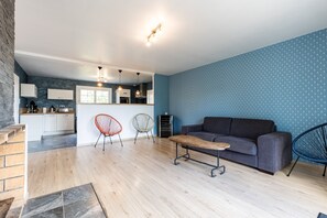 En moderne stue med sofa, sofabord og to stole. Et køkken kan ses i baggrunden med skabe og bordplade.