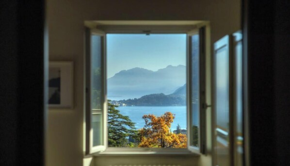 A view through an open window of a lake, mountains, and autumn foliage.