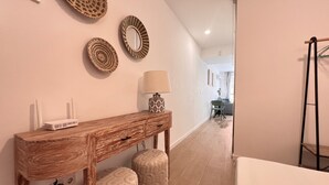 A hallway with a wooden console table, two ottomans, a lamp, and wall decor.