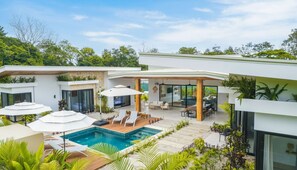 Een modern huis met een zwembad, terras en weelderige groene beplanting.