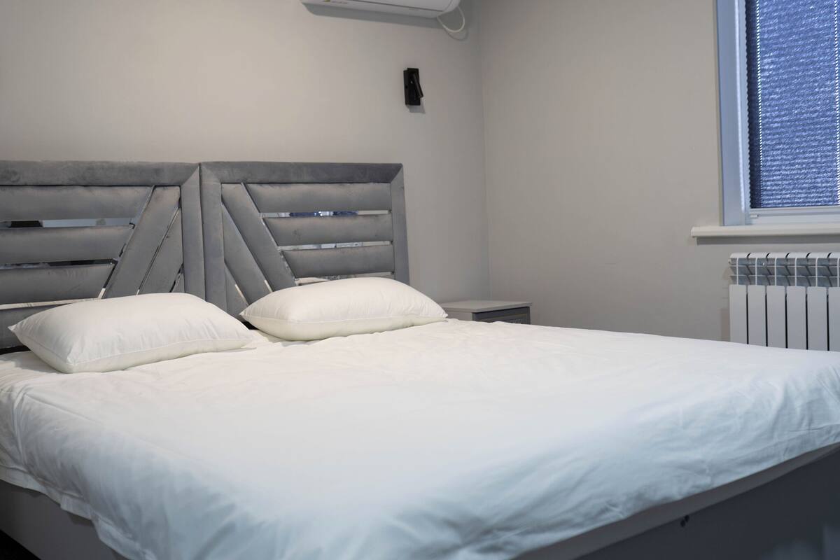 A bed with a grey upholstered headboard, white bedding, and two bedside tables.