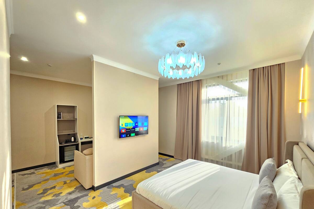 A hotel room with a bed, a TV mounted on the wall, a desk, and a wardrobe.