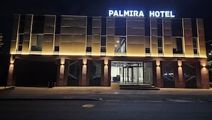 Exterior del hotel Palmira, con un diseño moderno, que cuenta con amplias ventanas y un llamativo letrero iluminado.