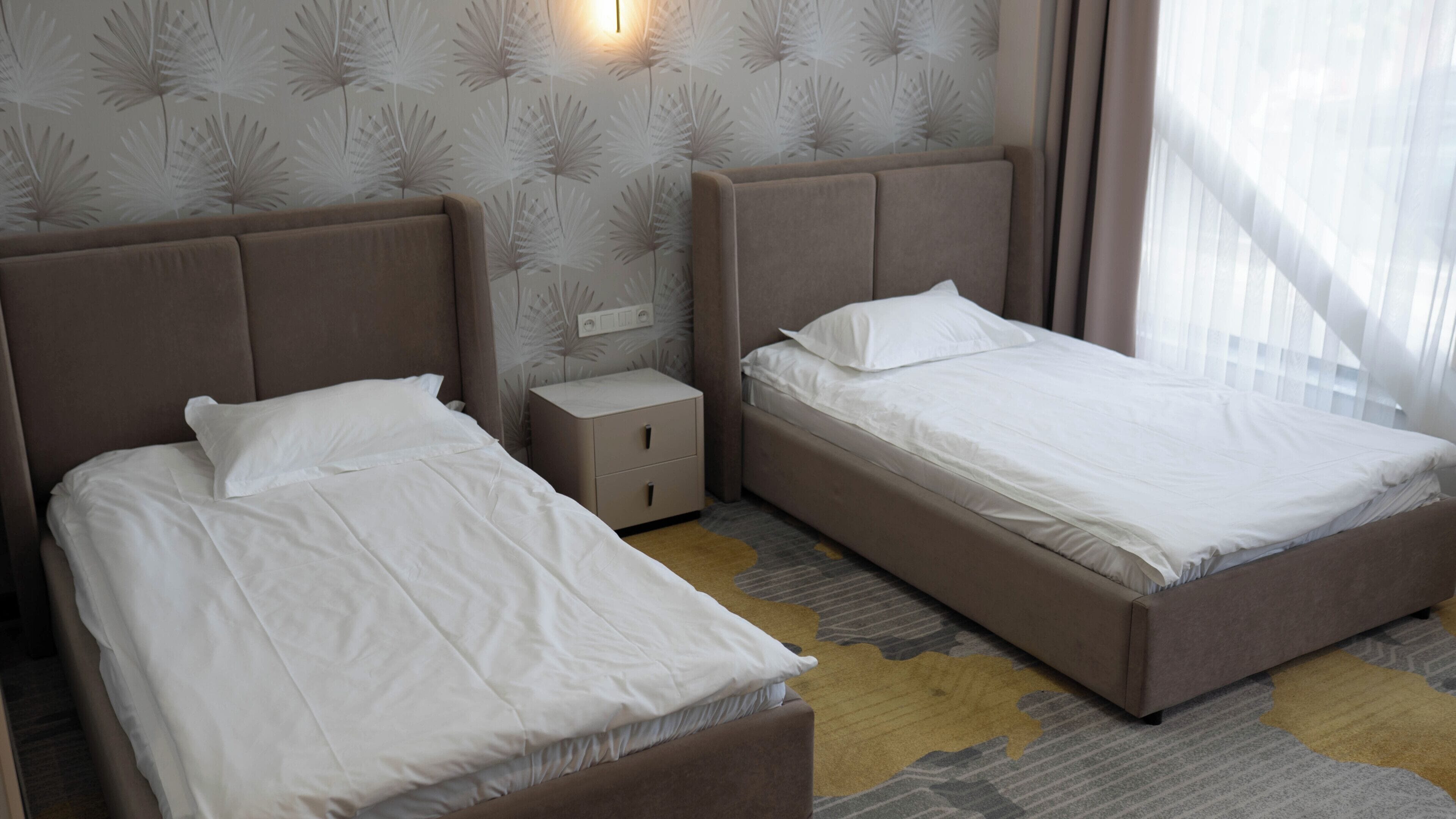 A hotel room with two beds, a nightstand, and a wall with a leaf pattern.