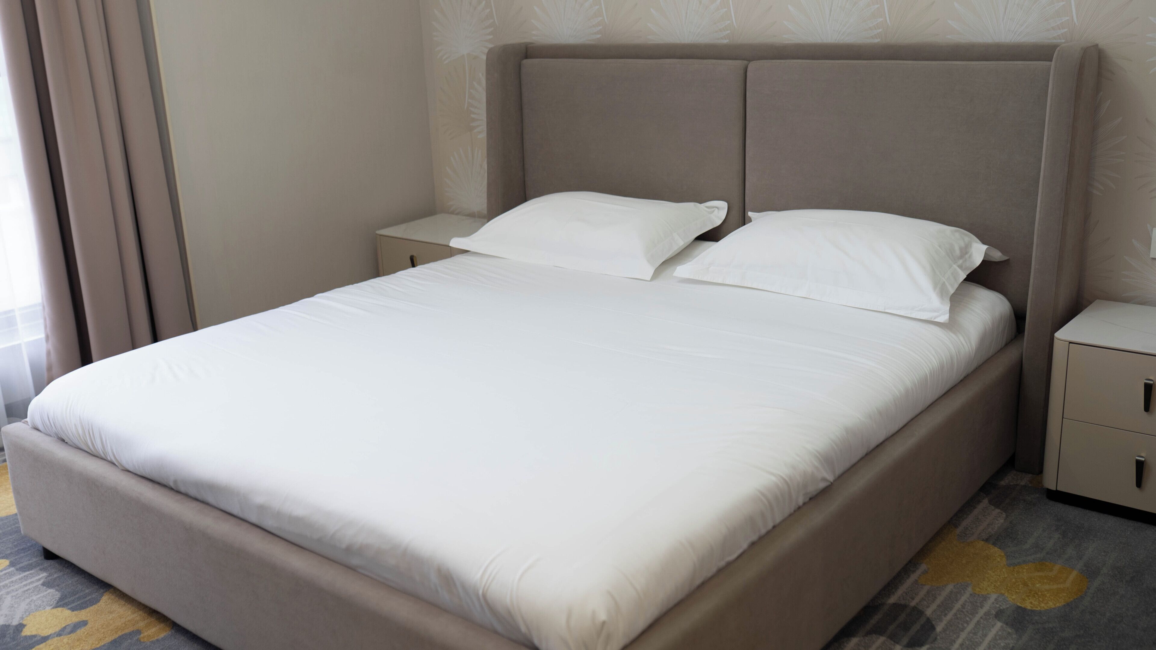 Una cama bien hecha con sábanas blancas, cabecera y mesita de noche con cajón.