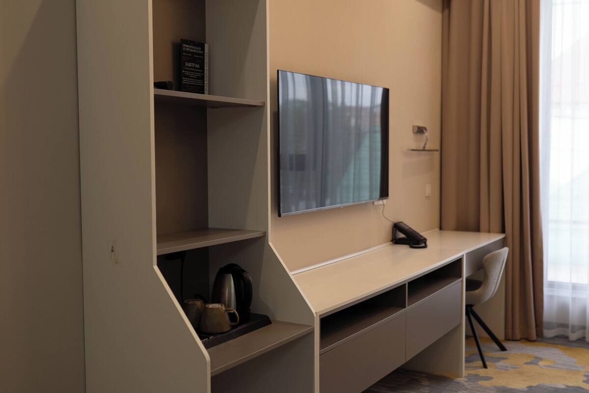 A hotel room with a flat-screen TV mounted on the wall, a desk with a telephone, and a chair.