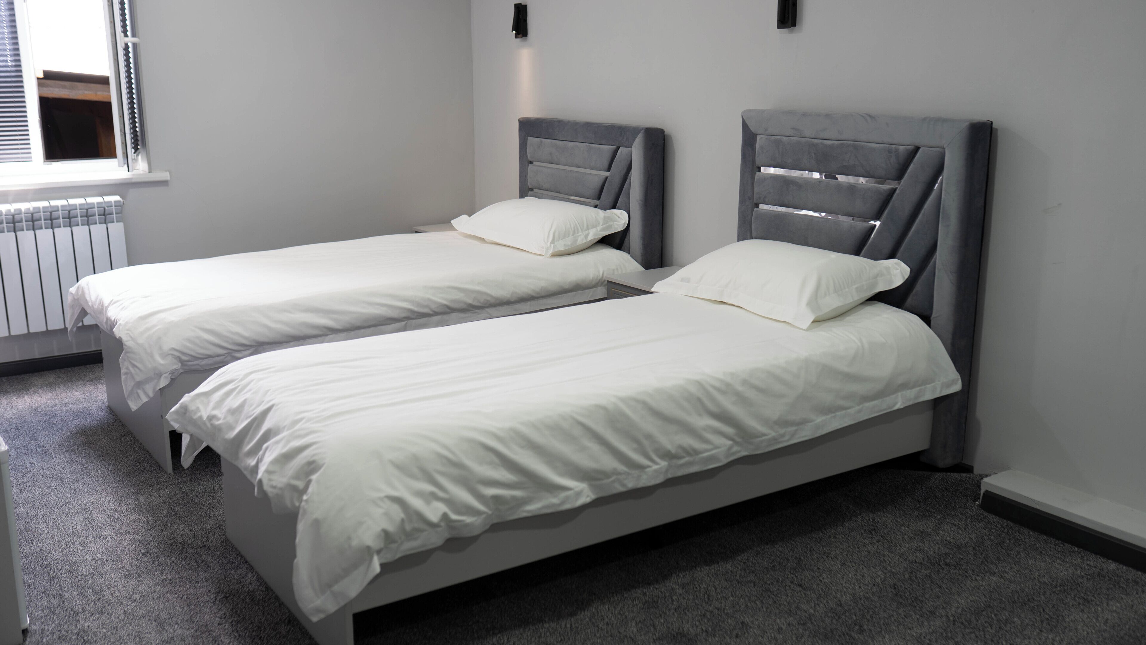 A room with two single beds, a radiator, and a window with blinds.