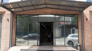 A building entrance with a glass door, a metal roof, and a brick facade. - Palmira Hotel Bishkek (Bishkek)
