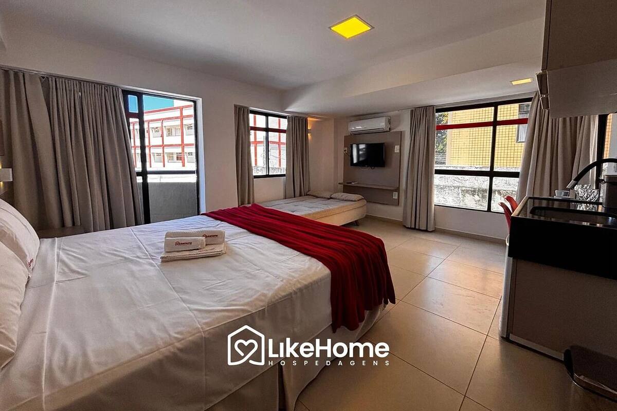 Une chambre d’hôtel avec deux lits, une télévision, une kitchenette et de grandes fenêtres avec des rideaux.