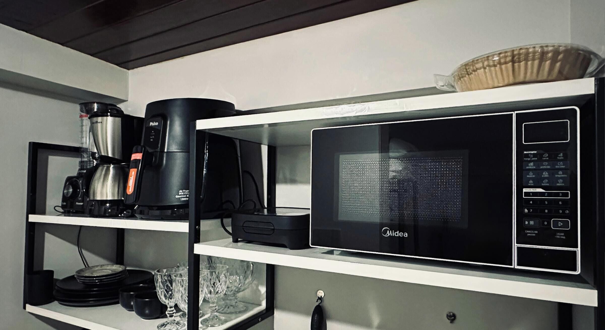 A kitchen with a coffee maker, microwave, and glassware on shelves.