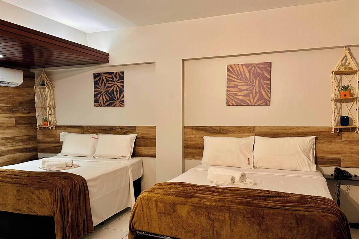 Une chambre d’hôtel avec deux lits, des têtes de lit en bois et un climatiseur fixé au mur.