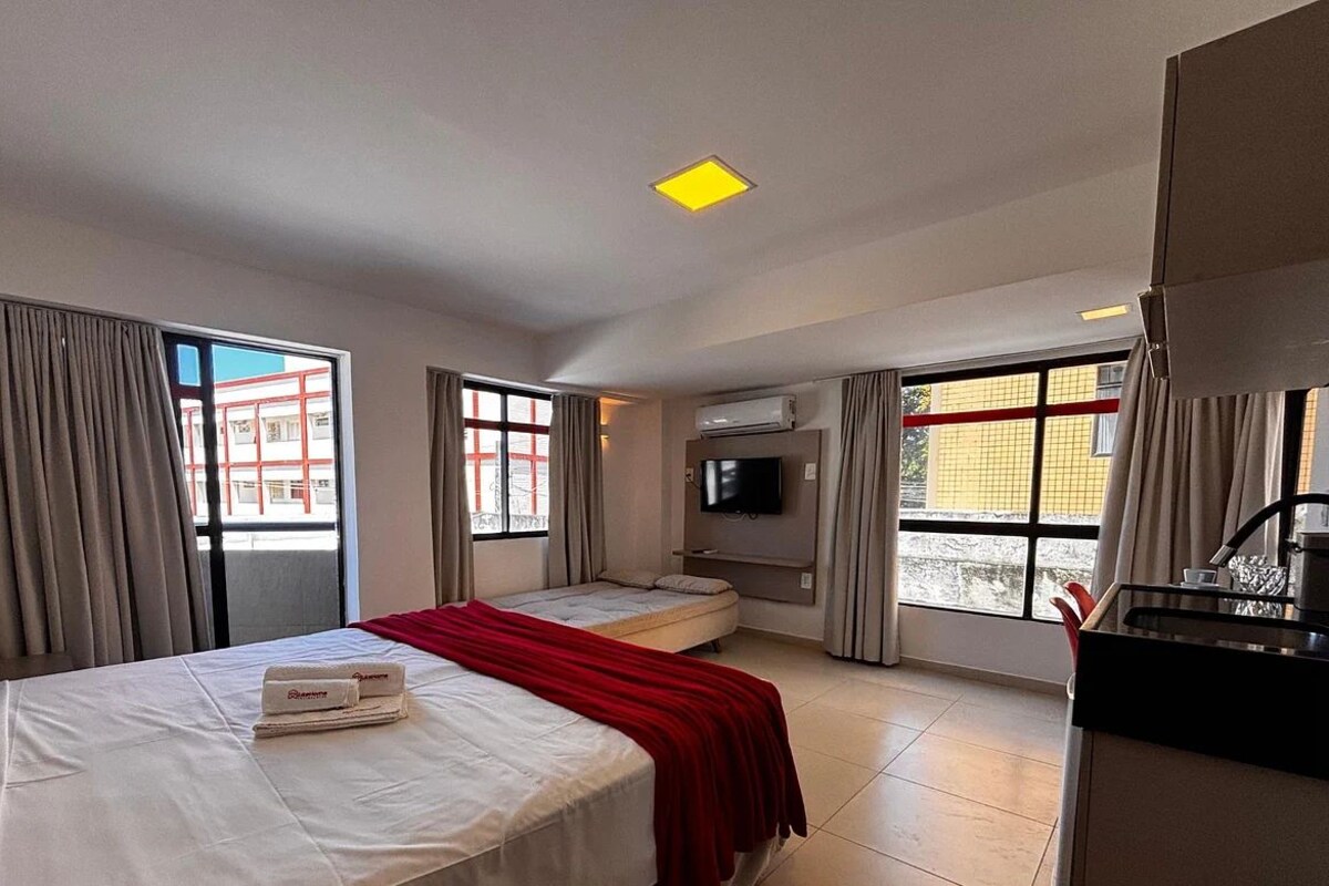 Une chambre d’hôtel avec deux lits, une télévision, une kitchenette et de grandes fenêtres avec des rideaux.