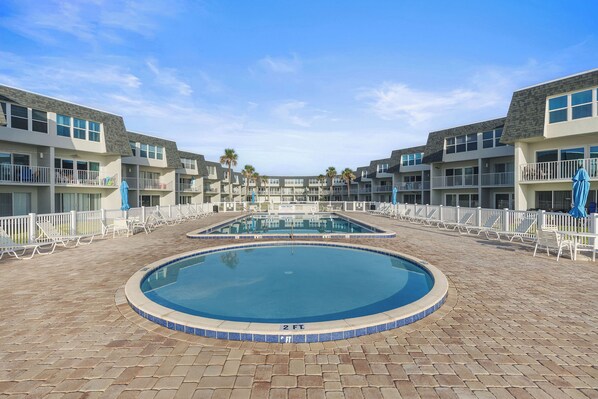 Un hotel con piscina central rodeada de sillas de descanso y sombrillas, con varios pisos y balcones.