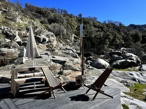 A wooden deck with two lounge chairs and a table, a stone fireplace, and a rocky hillside in the background. - Paradise Ranch Inn - All Tents (Three Rivers)