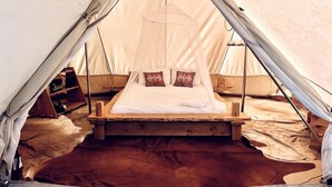 A tent with a bed, pillows, and a hanging light fixture.