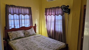 Een slaapkamer met een bed, gordijnen, een airconditioner en een ventilator.
