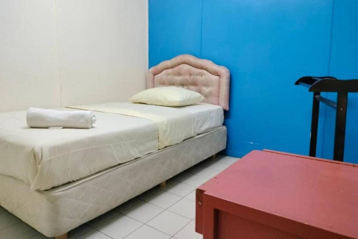 Ein kleines Zimmer mit einem Einzelbett, blauer Wand und rotem Tisch.