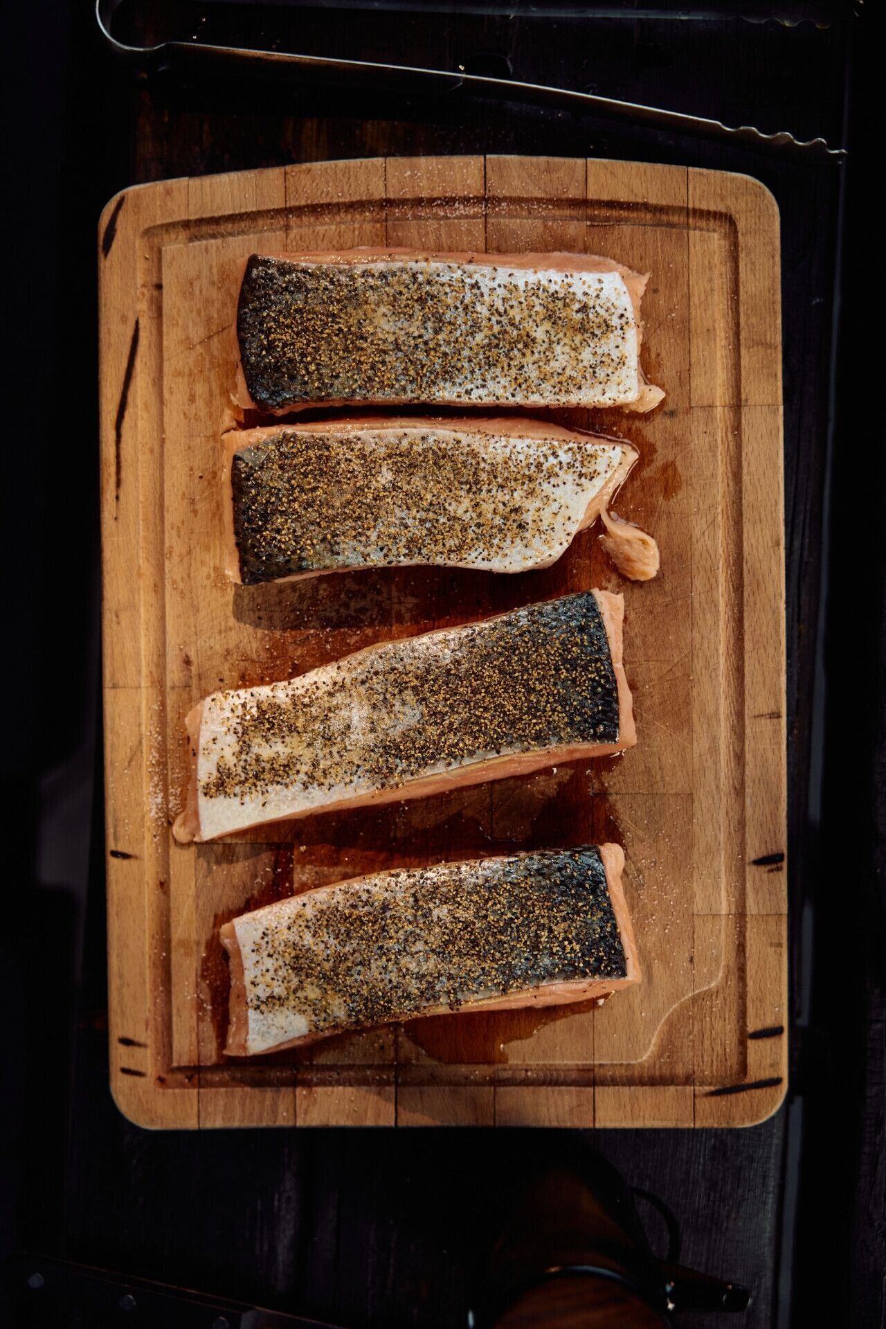 Four salmon fillets on a wooden cutting board.