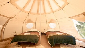 Een tent met twee bedden, elk voorzien van een groene spreideken en kussens, en een raam aan de zijkant.