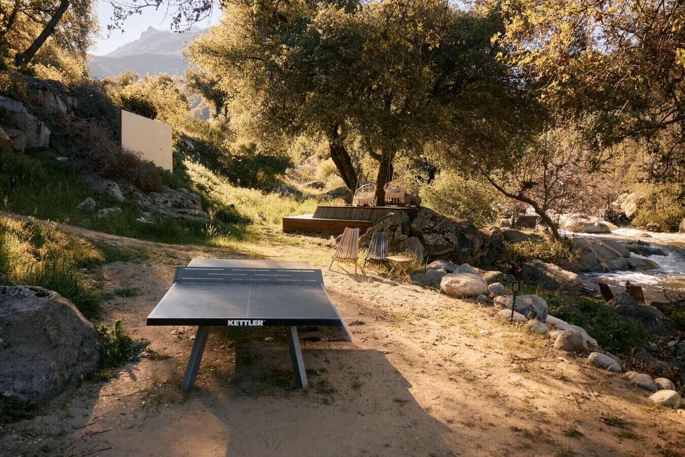 Mesa de ping pong en un entorno natural, con un banco y sillas cerca.