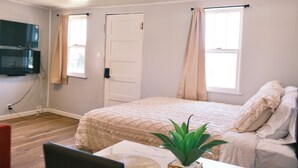 A bedroom with a bed, a plant, a TV mounted on the wall, and a window with curtains. - Stylish Studio Cabin in St. Ignace – Near Mackinac Ferry, WiFi & AC (St. Ignace)