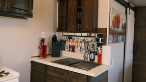 A kitchen with a built-in sink, dark wooden cabinets, a coffee maker, and a hanging towel rack. - Stylish Studio Cabin in St. Ignace – Near Mackinac Ferry, WiFi & AC (St. Ignace)
