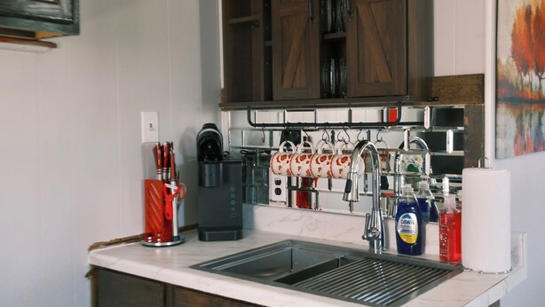 A kitchen with a sink, coffee maker, kettle, and various utensils. - Stylish Studio Cabin in St. Ignace – Near Mackinac Ferry, WiFi & AC (St. Ignace)
