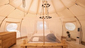 Een tent met een bed, een houten dressoir, een kachel en twee ramen.