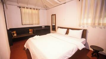 A bedroom with a large bed, a bedside table, a bench with cushions, a mirror, and a window with curtains.