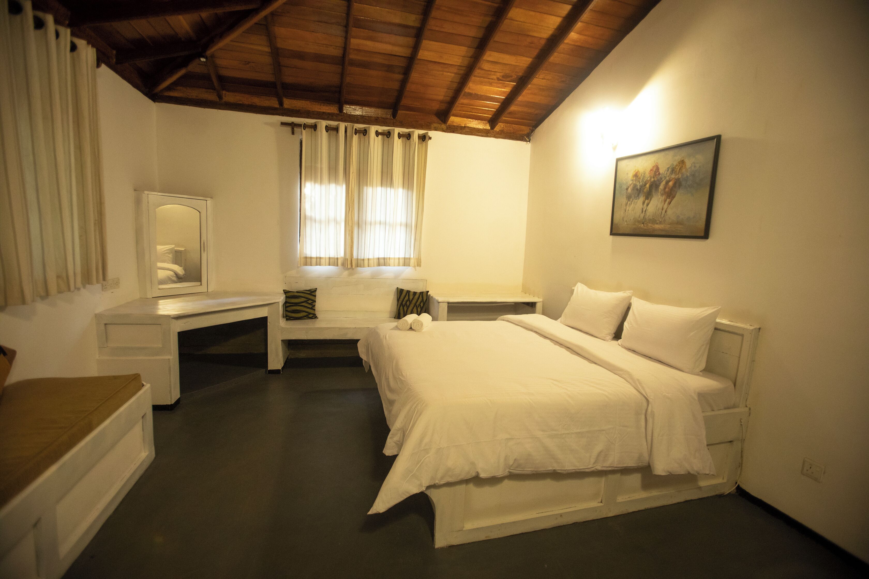 A bedroom with a bed, a desk, a chair, a window with curtains, and a painting on the wall.