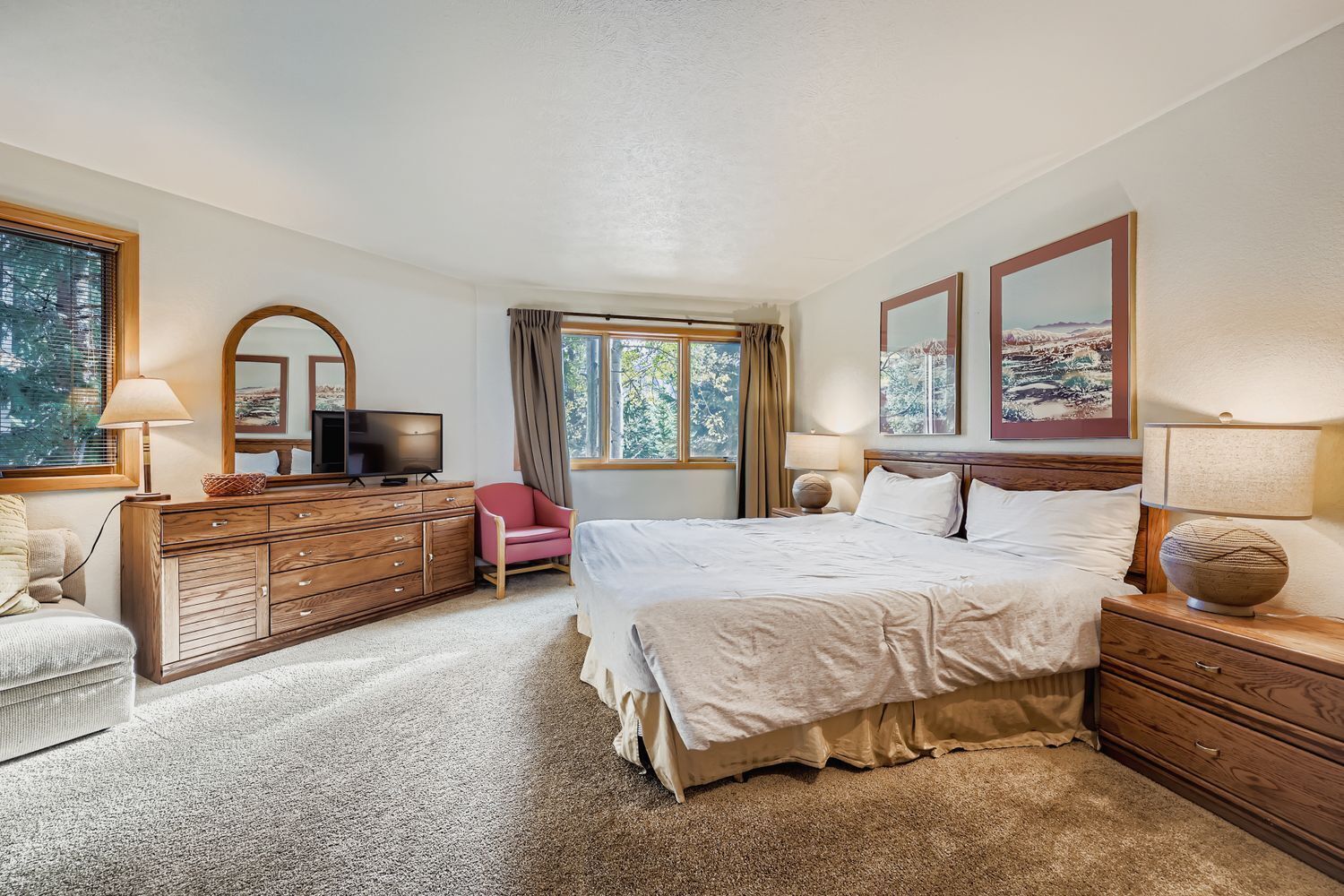 A bedroom with a large bed, a wooden dresser, a television, and a chair.