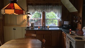 Una cocina con armarios de madera, estufa, fregadero y ventana con cortinas.