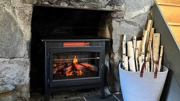 A stone fireplace with a black wood-burning stove, logs in a basket, and a patterned rug on the floor.