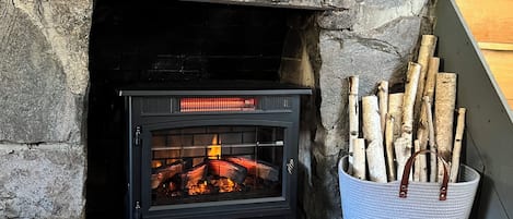 A stone fireplace with a black wood-burning stove, logs in a basket, and a patterned rug on the floor.