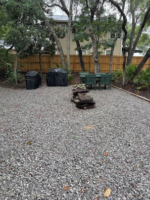 A gravel patio with a fire pit, green chairs, and two covered grills.