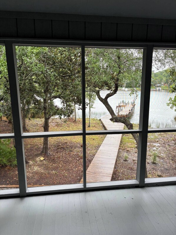 A room with large windows offering a view of a dock and trees by a lake. - Navarre’s Paradise (Navarre)